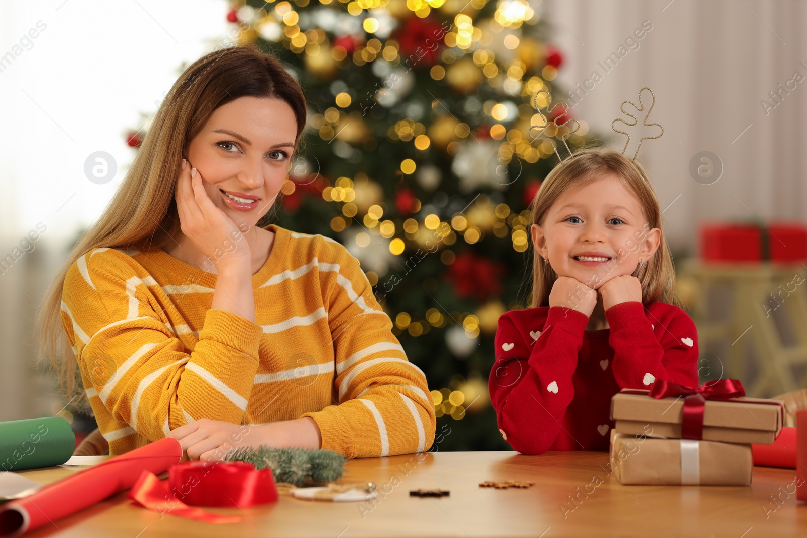 Photo of Christmas presents wrapping. Happy mother and her little daughter at table with gift boxes in room