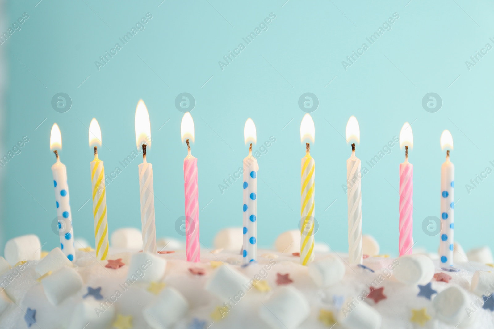 Photo of Birthday cake with burning candles on turquoise background, closeup