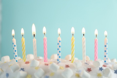 Photo of Birthday cake with burning candles on turquoise background, closeup