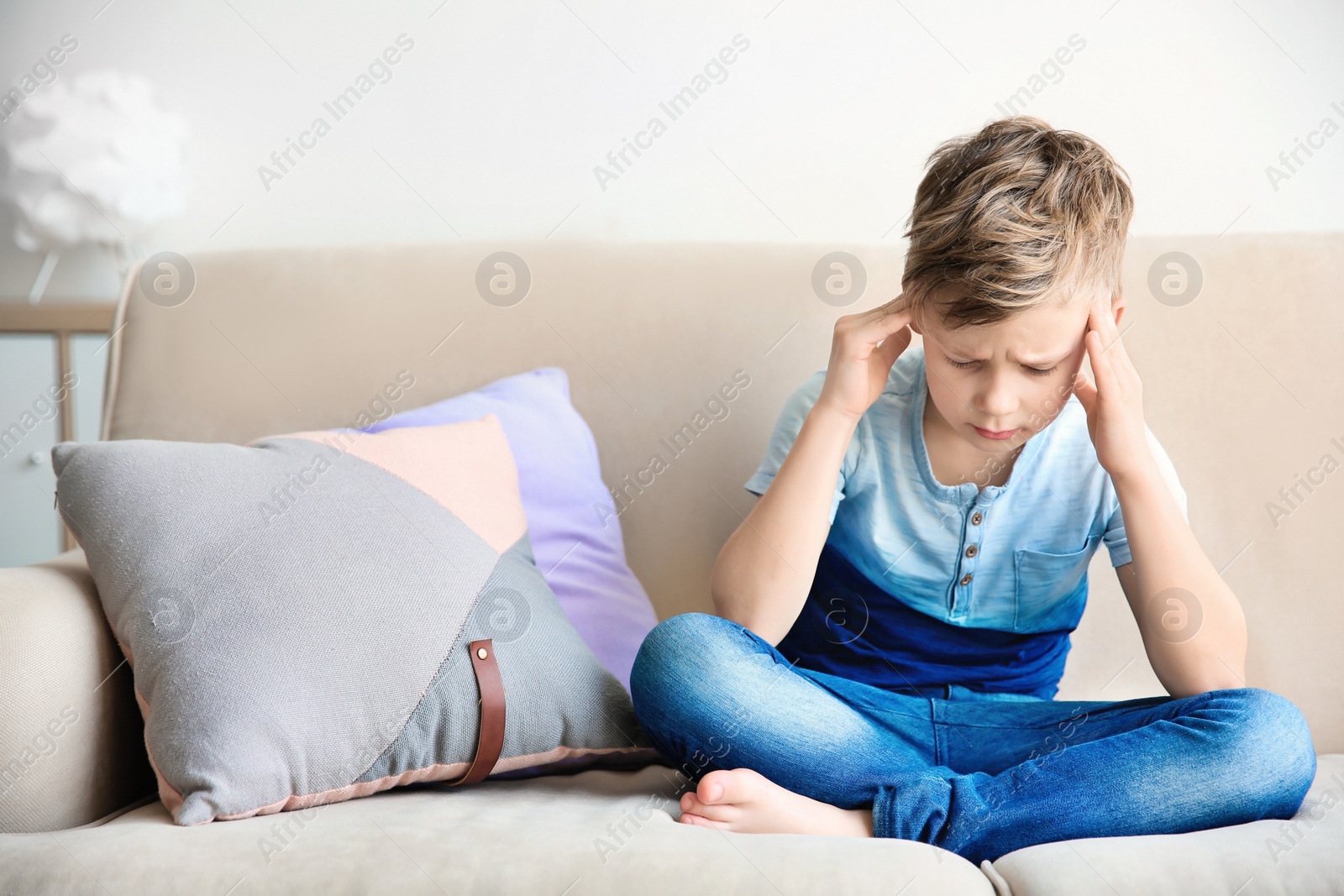 Photo of Little boy suffering from headache while sitting on couch at home