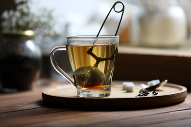 Photo of Cup of freshly brewed tea with snap infuser and sugar cubes on wooden table indoors