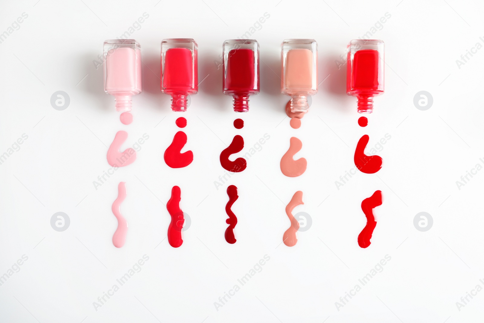 Photo of Spilled colorful nail polishes and bottles on white background, top view