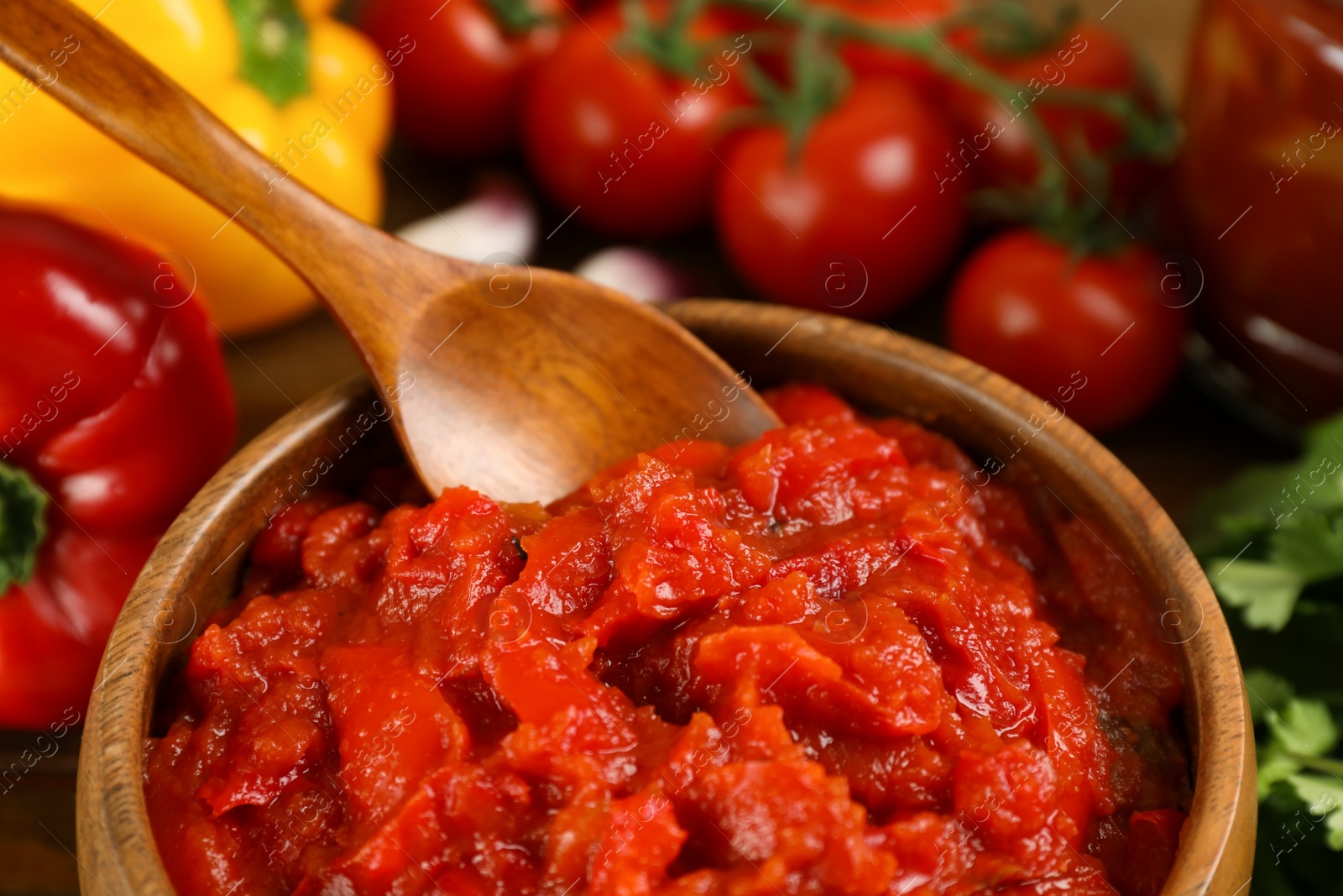 Photo of Delicious lecho with spoon in wooden bowl and fresh vegetables, closeup