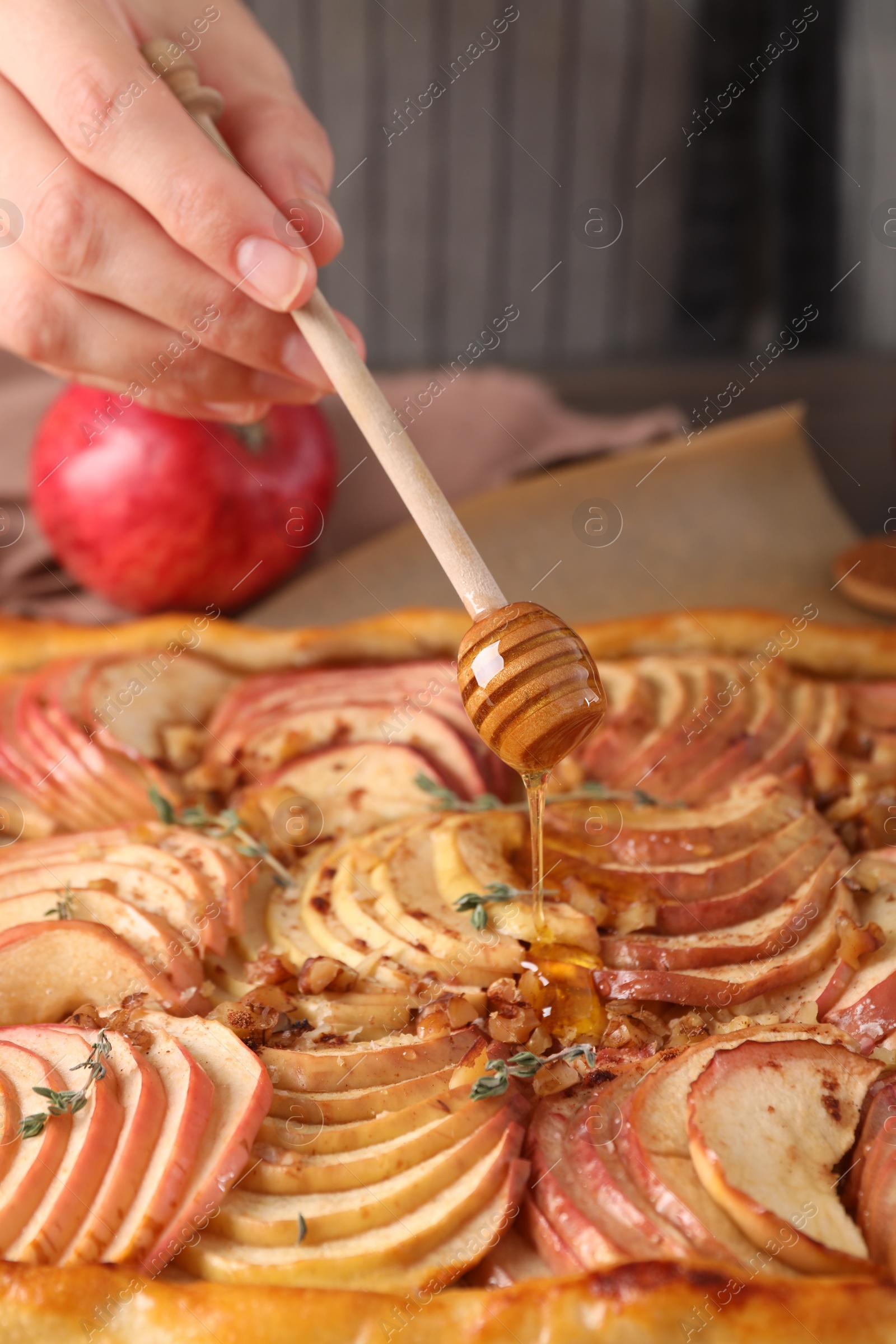Photo of Woman adding honey to freshly baked apple pie at table, closeup