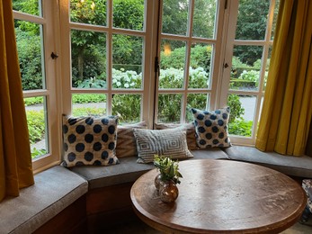 Photo of Wooden table near bay window seat with cushions in cozy room. Interior design