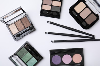 Many different eye shadow palettes and professional makeup brushes on white background, flat lay