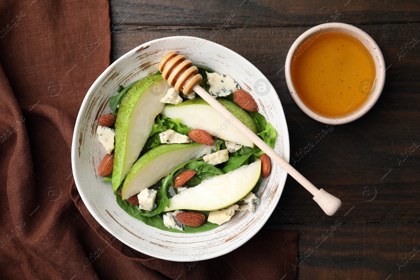 Photo of Delicious pear salad in bowl, honey and dipper on wooden table, top view