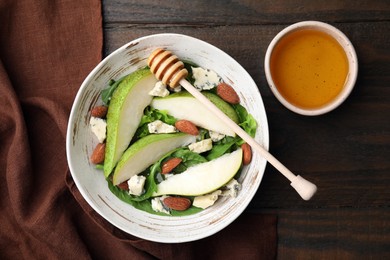 Photo of Delicious pear salad in bowl, honey and dipper on wooden table, top view