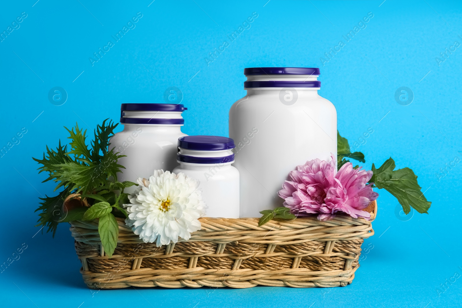 Photo of White medical bottles, arugula and flowers in wicker tray on light blue background