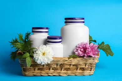 Photo of White medical bottles, arugula and flowers in wicker tray on light blue background