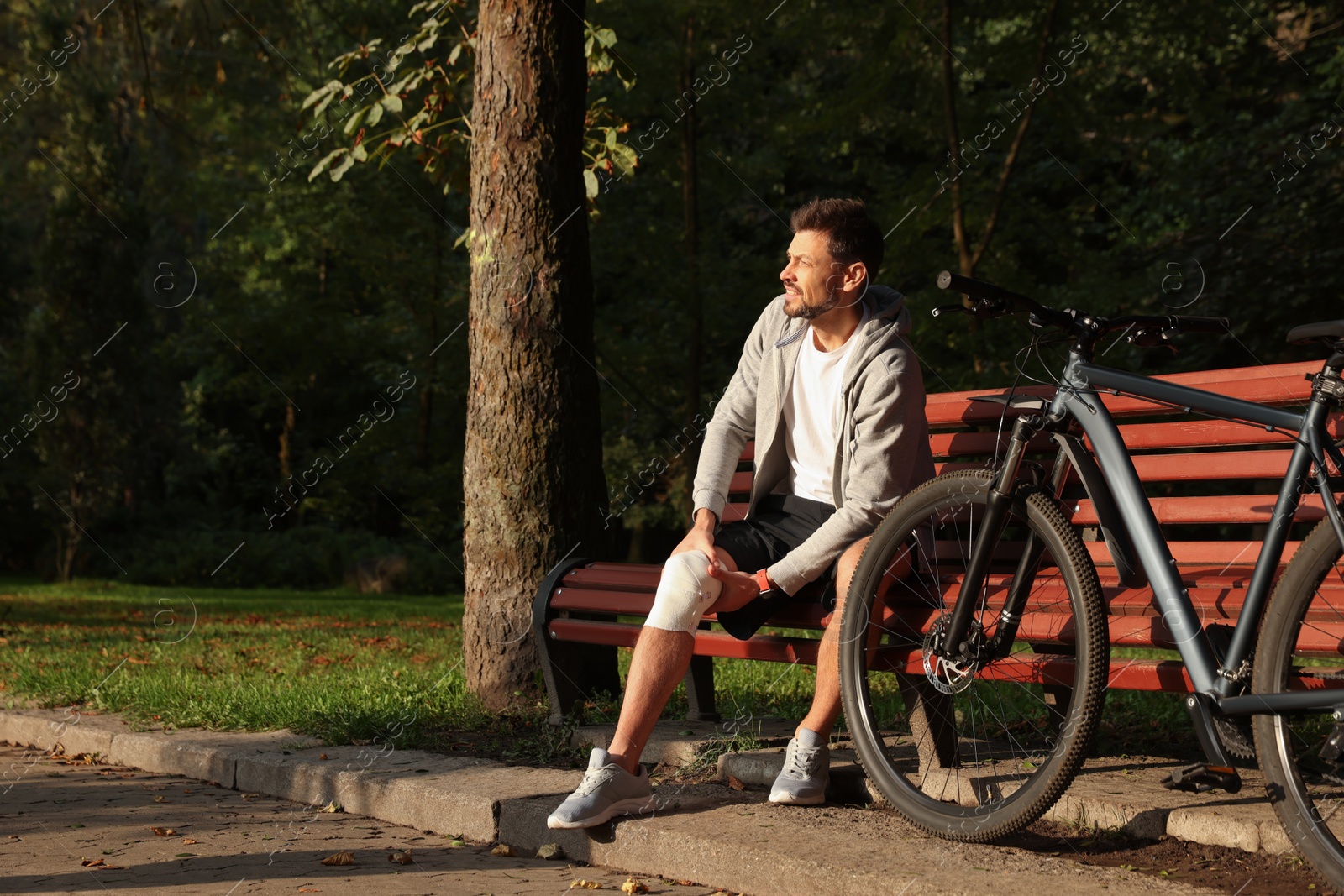 Photo of Man with injured knee on bench near bicycle outdoors