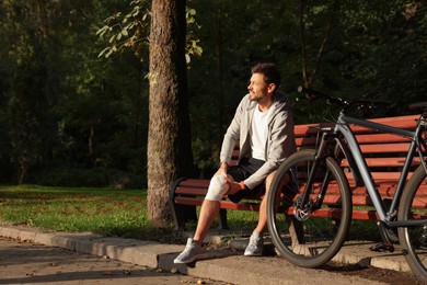 Man with injured knee on bench near bicycle outdoors