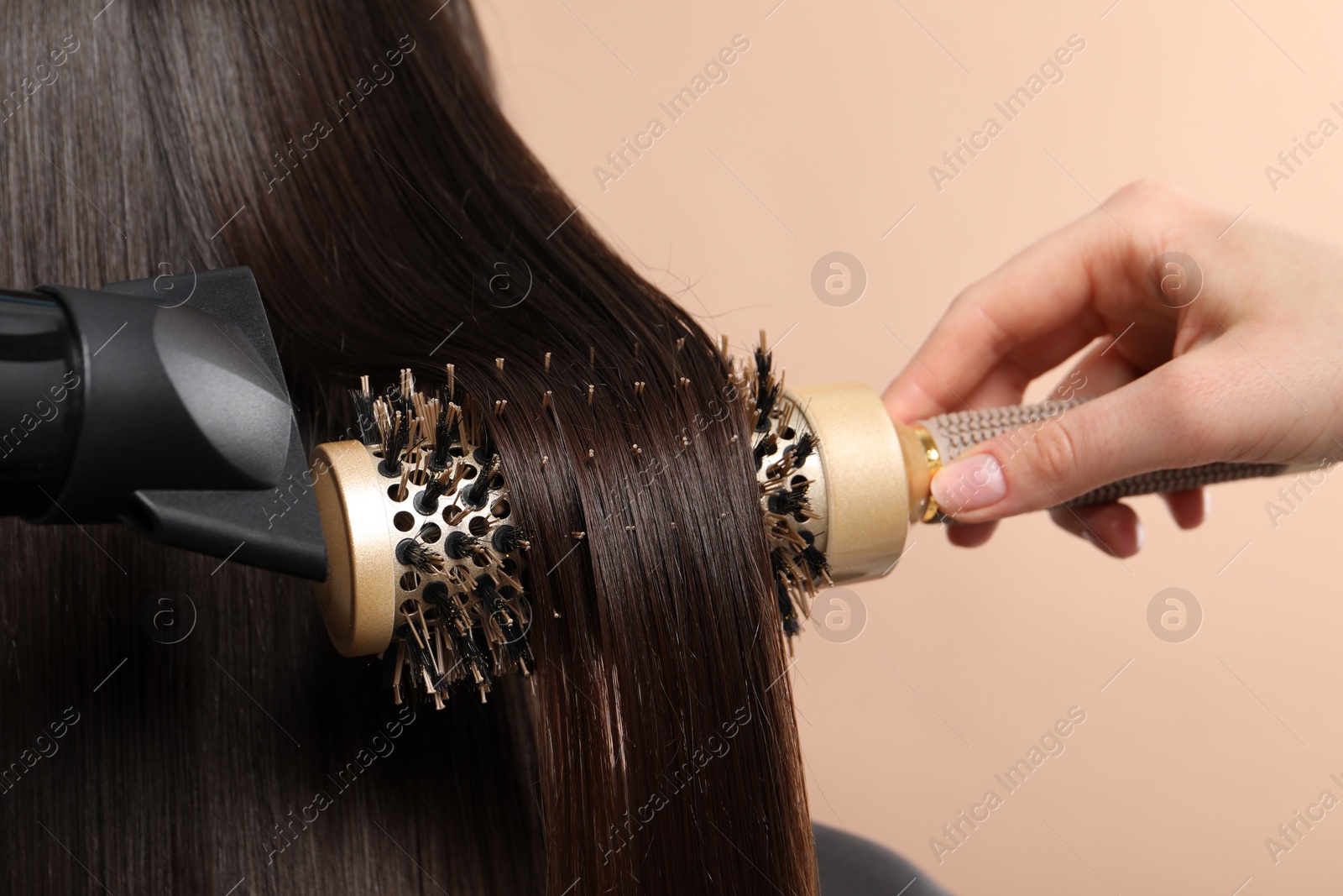 Photo of Hairdresser blow drying client's hair on beige background, closeup