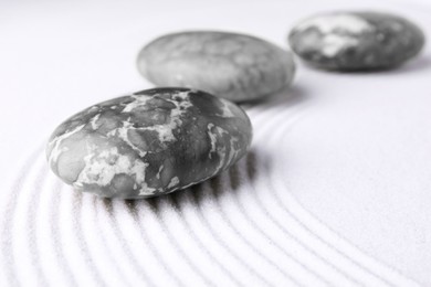 Photo of Zen garden stones on white sand with pattern, closeup