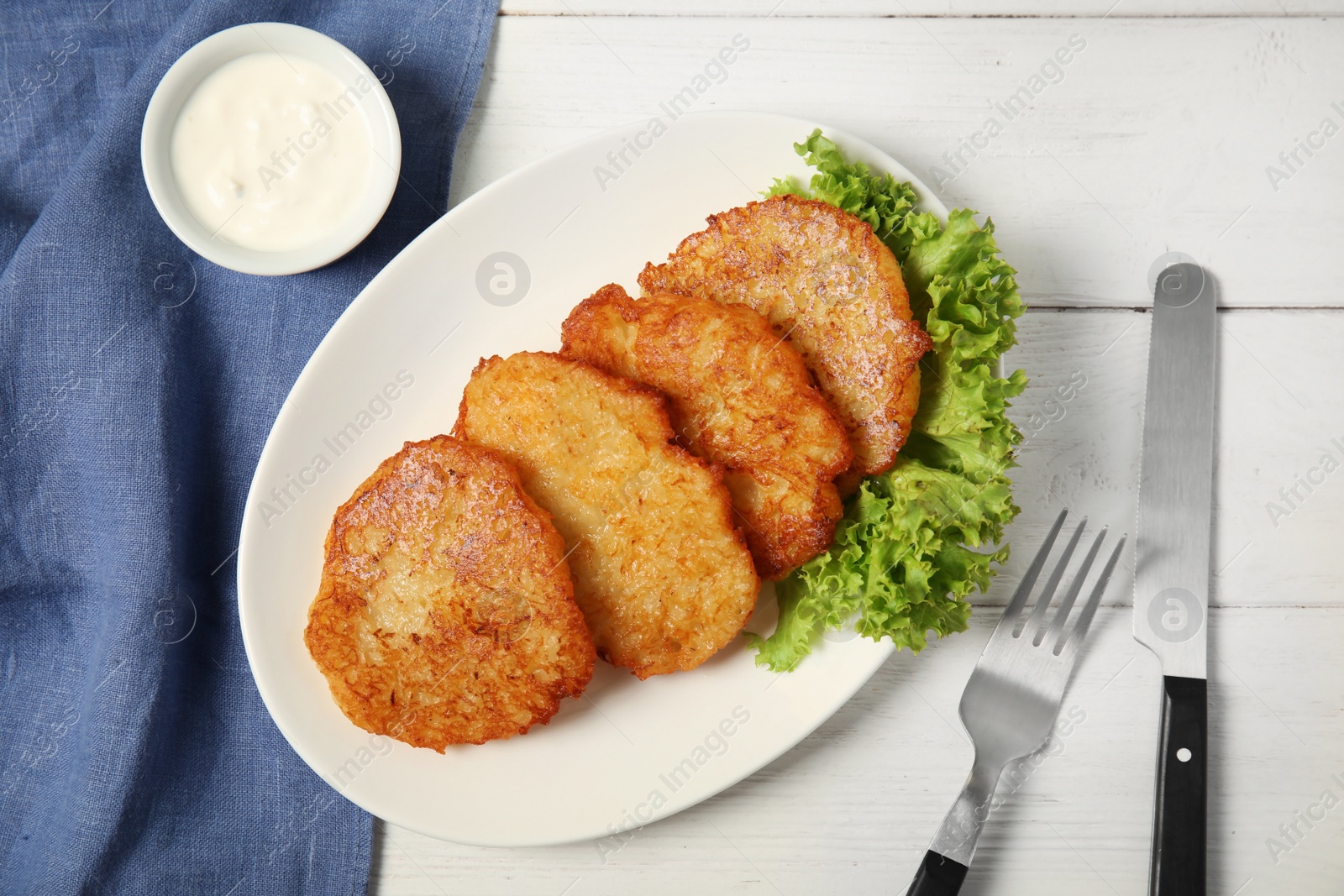 Photo of Plate with tasty potato fritters and sauce on wooden table, top view