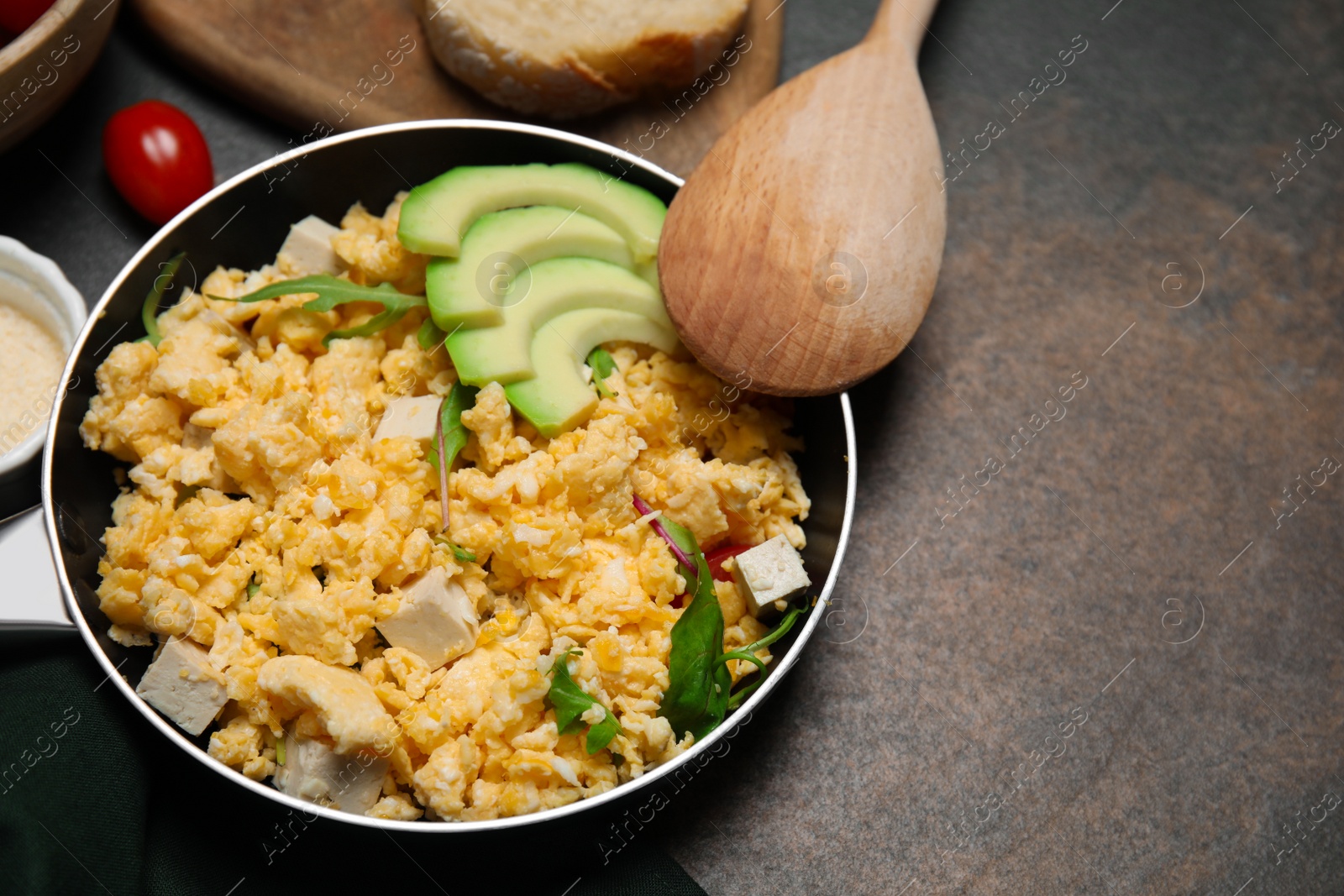 Photo of Frying pan with delicious scrambled eggs, tofu and avocado on textured table. Space for text