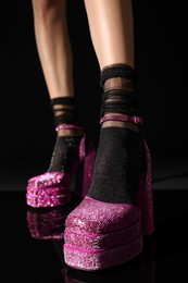 Photo of Woman wearing pink high heeled shoes with platform and square toes on black background, closeup