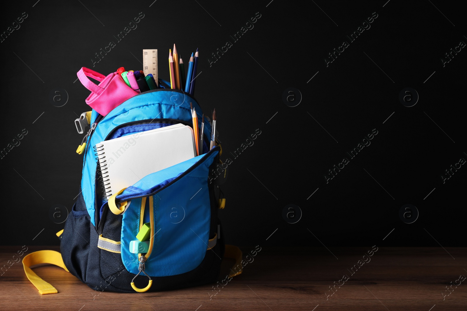 Photo of Backpack with different school stationery on wooden table near blackboard, space for text