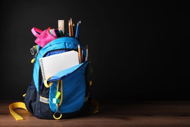 Photo of Backpack with different school stationery on wooden table near blackboard, space for text