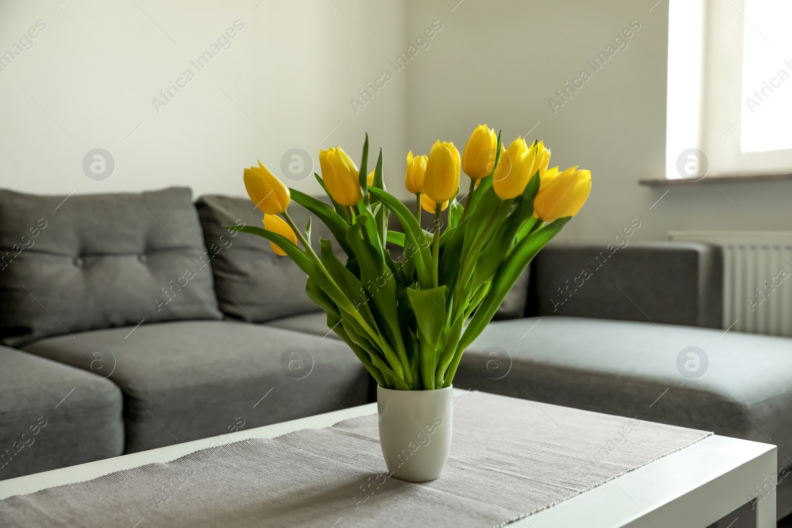 Photo of Bouquet of beautiful yellow tulips on table in living room