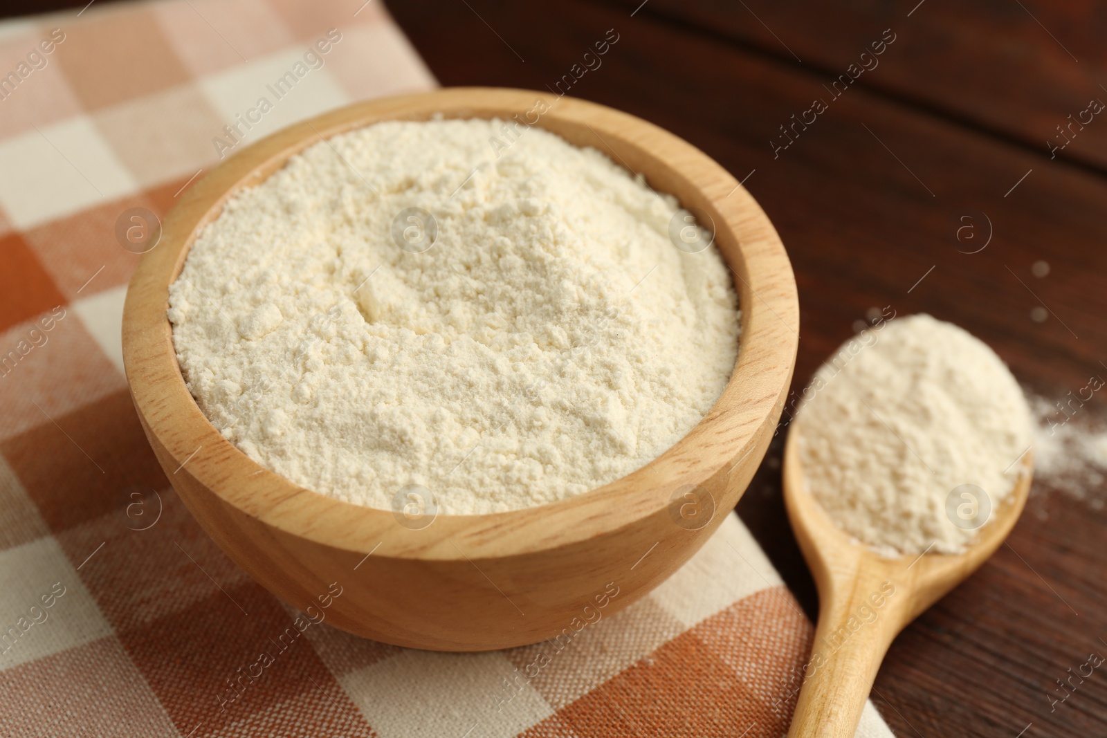 Photo of Baking powder in bowl and spoon on wooden table, closeup