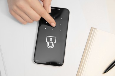 Woman unlocking smartphone with blocked screen at white table, closeup