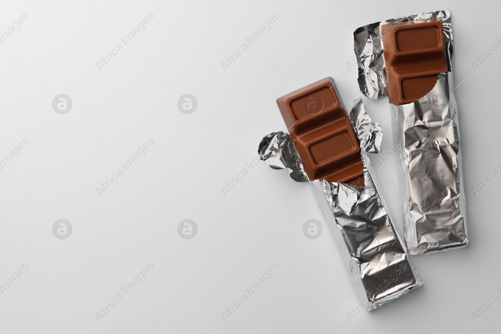 Photo of Delicious chocolate bars wrapped in foil on light blue background, flat lay. Space for text