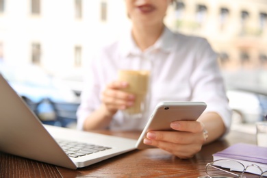 Photo of Young woman using mobile phone while working with laptop at desk, closeup