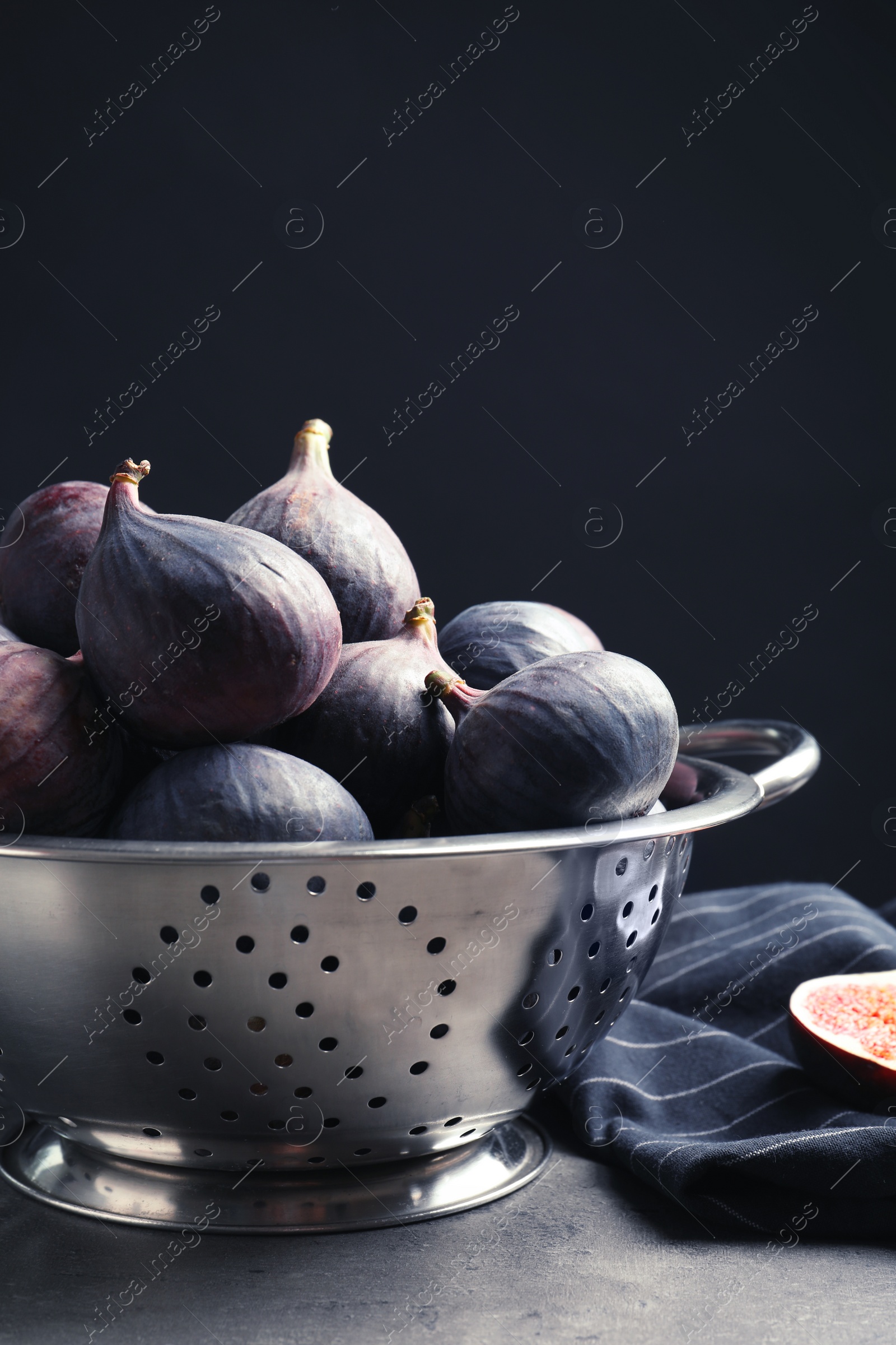 Photo of Colander with fresh ripe figs on table against black background