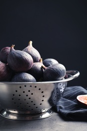 Photo of Colander with fresh ripe figs on table against black background