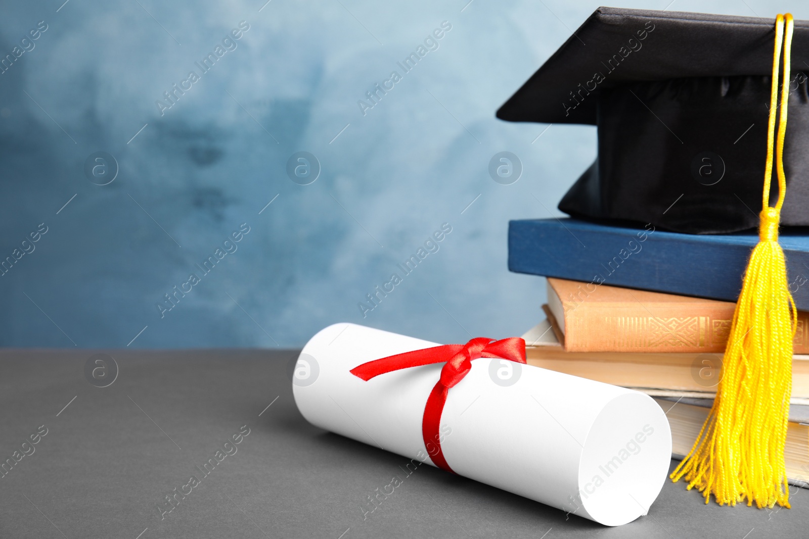 Photo of Graduation hat, books and student's diploma on grey table against light blue background. Space for text