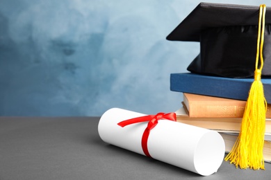 Graduation hat, books and student's diploma on grey table against light blue background. Space for text