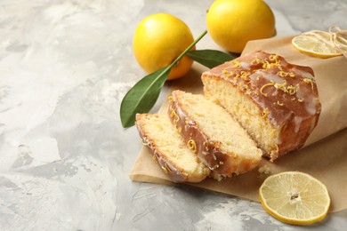 Photo of Cut tasty lemon cake with glaze and citrus fruits on light grey textured table, space for text