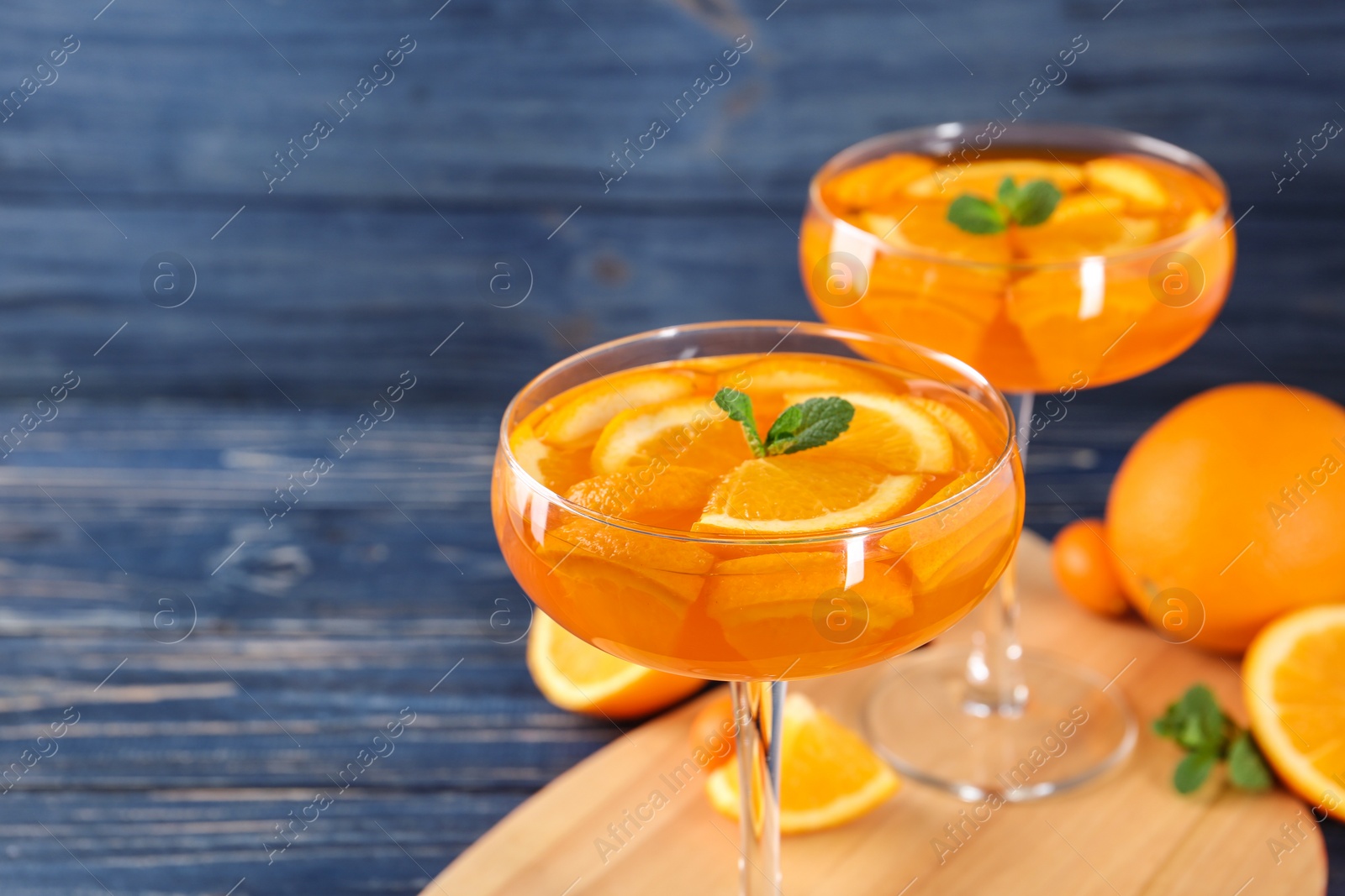 Photo of Dessert glasses of orange jelly served on blue wooden table, closeup. Space for text