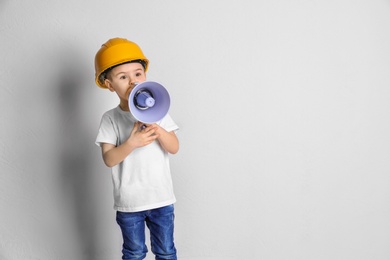Photo of Adorable little boy in hardhat with megaphone on light background