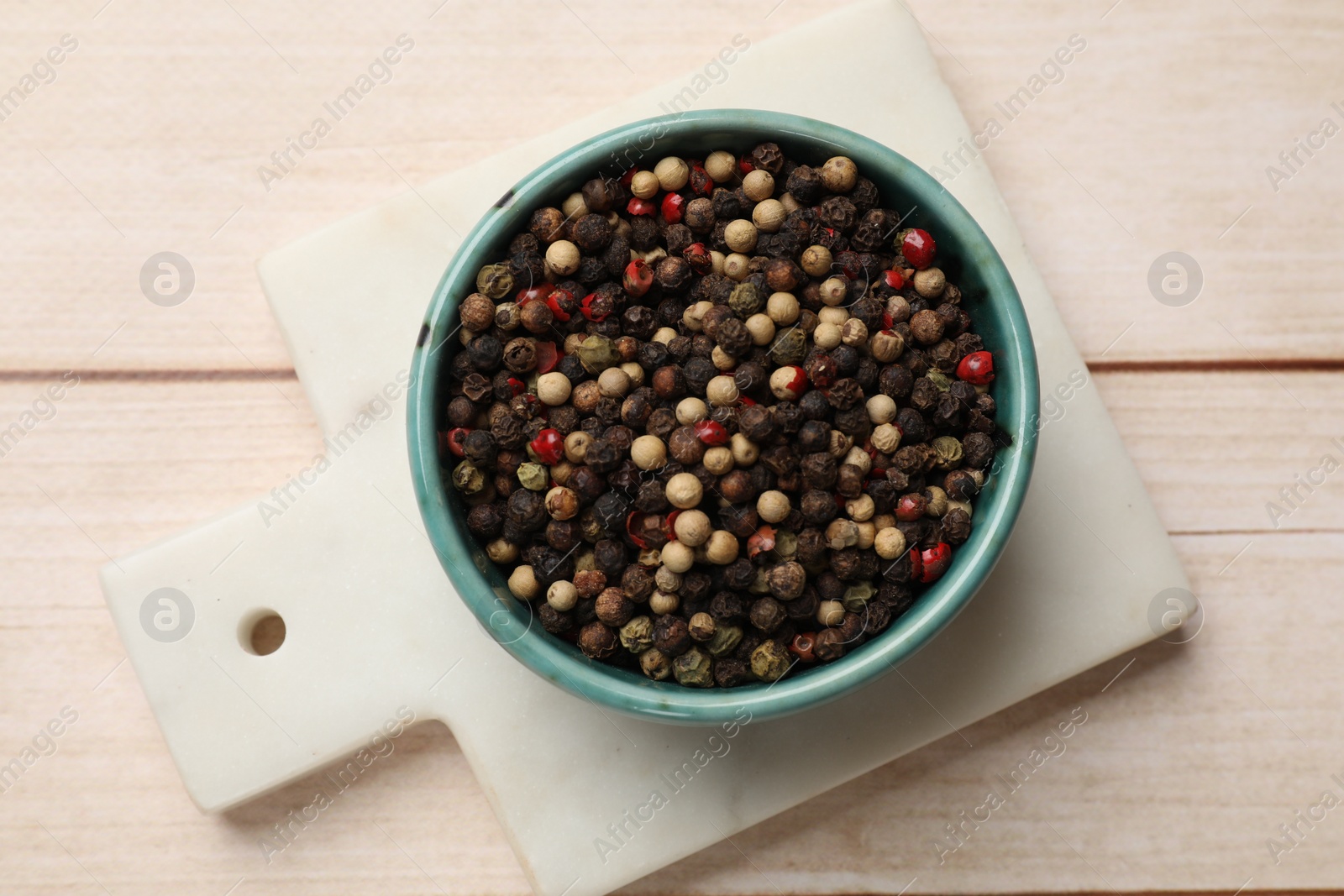 Photo of Aromatic spices. Different peppers in bowl on wooden table, top view