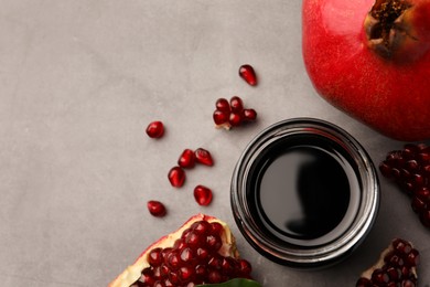 Photo of Glass jar of tasty pomegranate sauce and fresh ripe fruit on light grey table, flat lay. Space for text