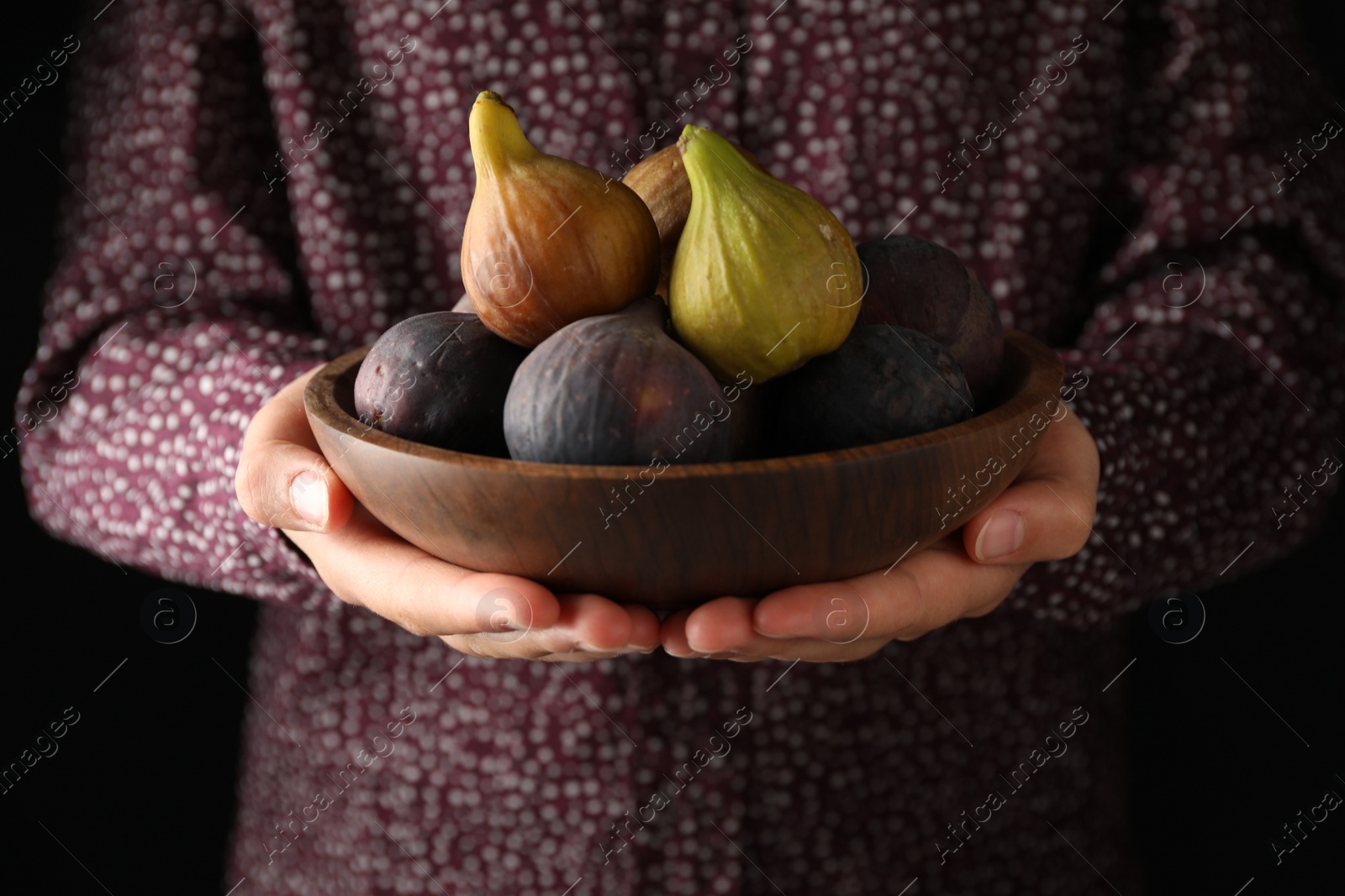 Photo of Woman holding bowl with tasty raw figs on black background, closeup