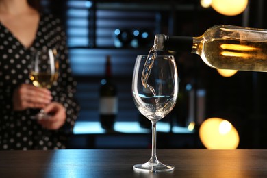 Pouring white wine from bottle into glass on bar counter. Space for text