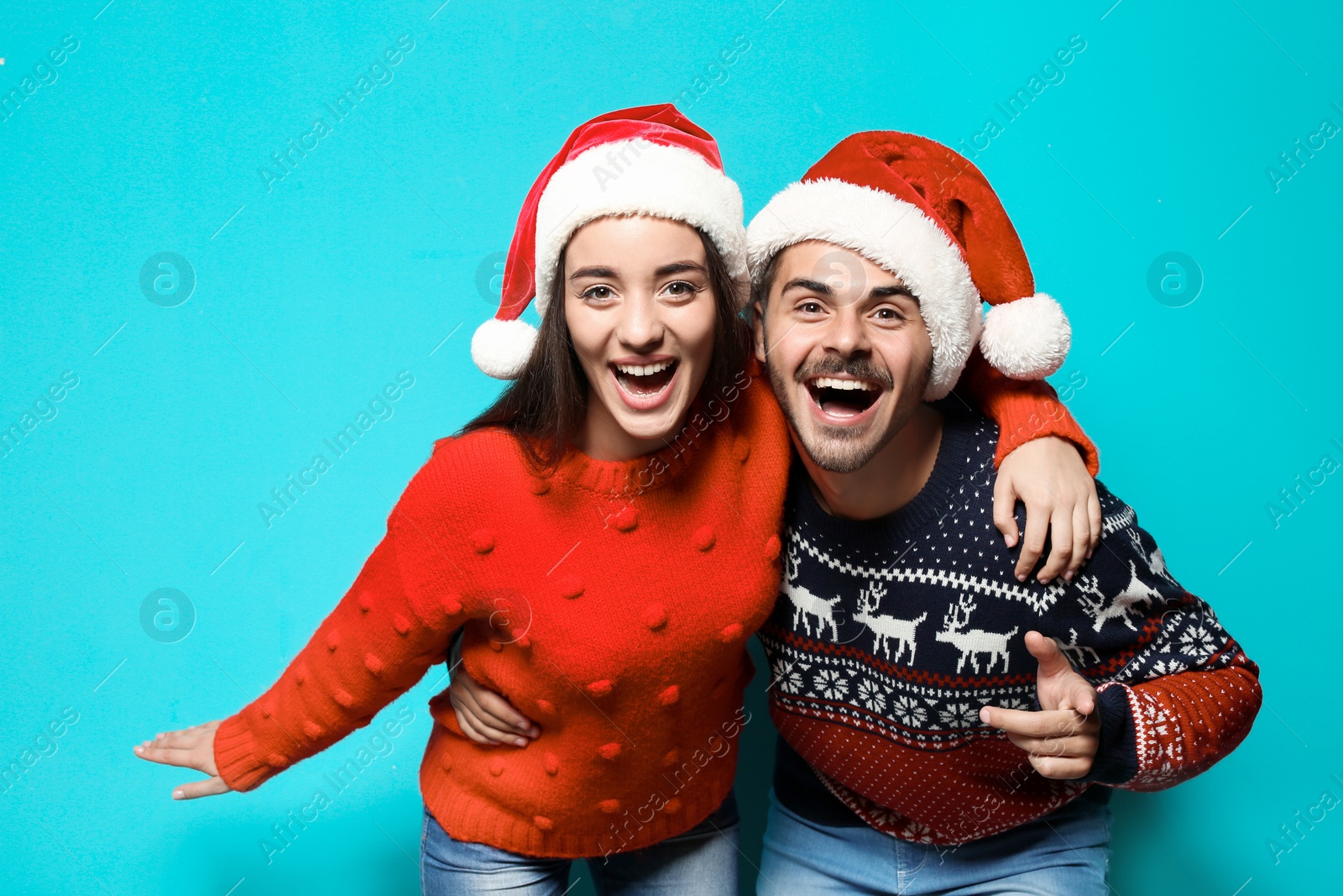 Photo of Young couple in warm sweaters and Christmas hats on color background