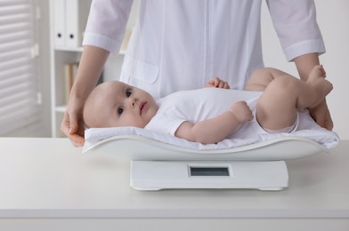 Pediatrician weighting cute little baby in clinic, closeup