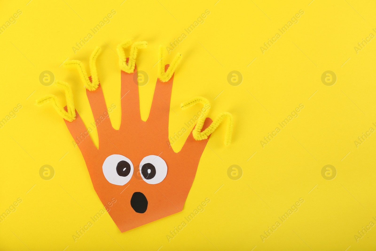 Photo of Funny orange hand shaped monster on yellow background, top view with space for text. Halloween decoration