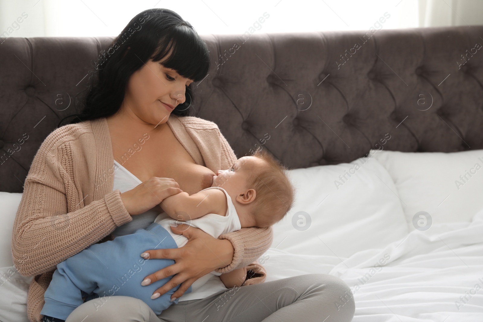 Photo of Woman breastfeeding her little baby on bed indoors