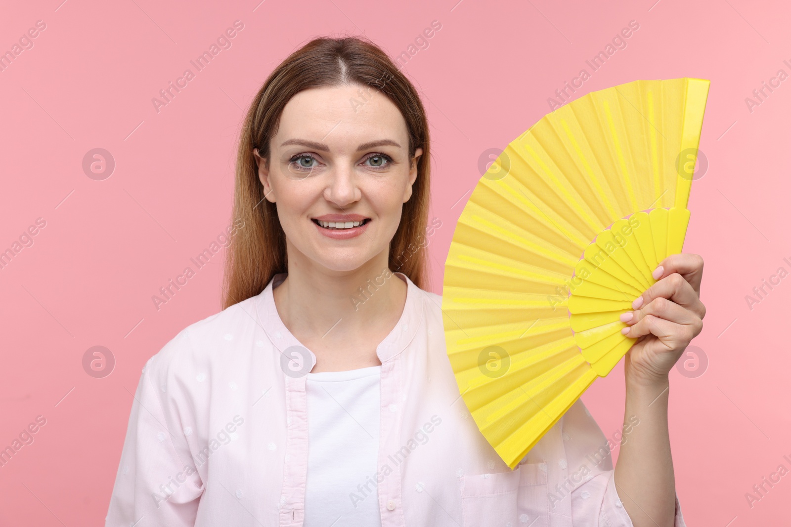 Photo of Happy woman with yellow hand fan on pink background