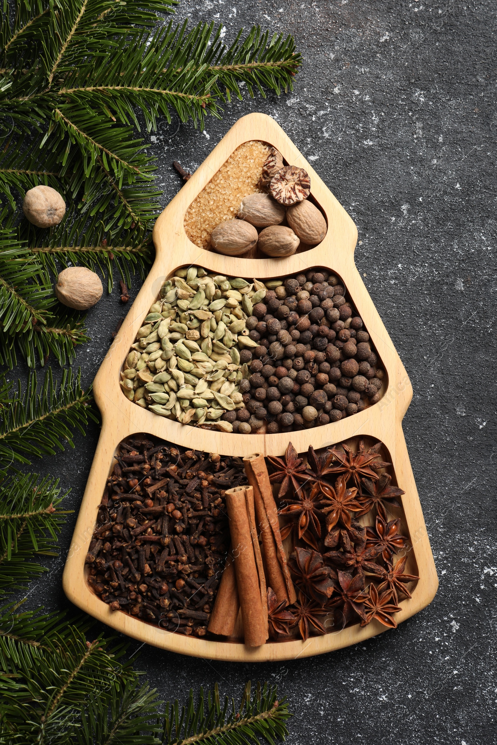 Photo of Different spices, nuts and fir branches on dark gray textured table, flat lay