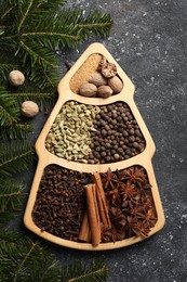 Photo of Different spices, nuts and fir branches on dark gray textured table, flat lay