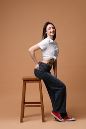 Smiling tattooed woman sitting on stool against beige background