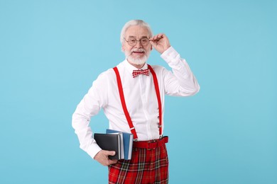 Portrait of stylish grandpa with glasses, bowtie and books on light blue background