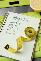 Photo of Notebook with products of low glycemic index, calculator, measuring tape and lemon, closeup