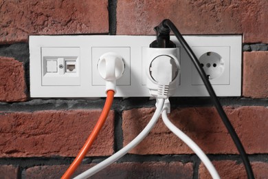 Photo of Many different electrical power plugs in sockets on red brick wall
